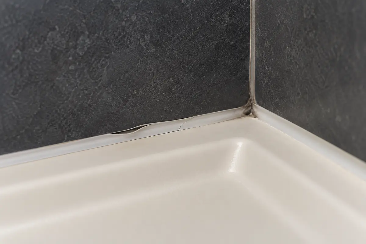 Joint souple fissuré et décollé à la jonction d’un receveur de douche et d’un mur carrelé